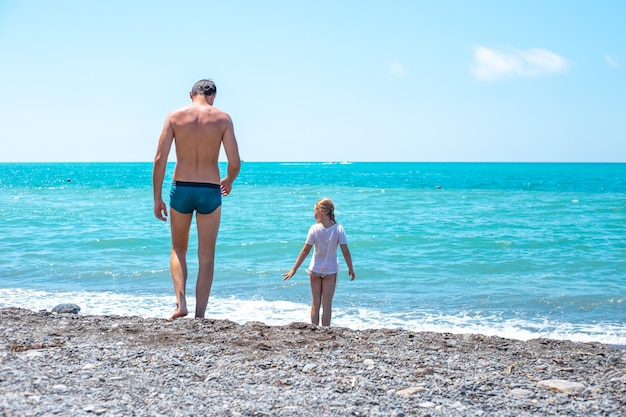 Little girl with her father on the coast pebble beach and blue sea summer vacation and travel