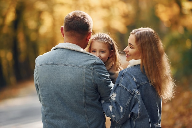 Little girl with her parents Happy family is in the park at autumn time together