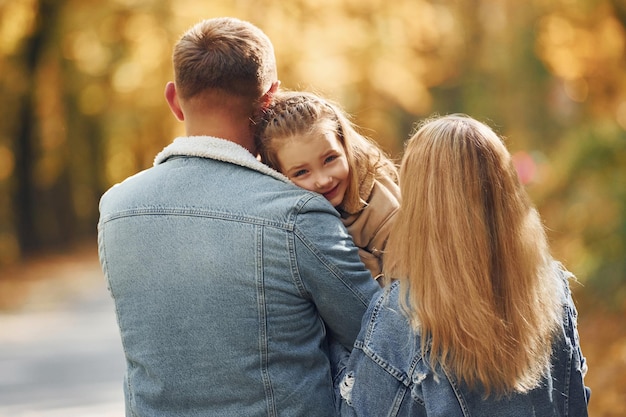 Little girl with her parents Happy family is in the park at autumn time together