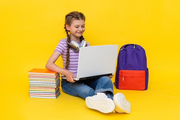 A little girl with a laptop is engaged in lessons at an online school Distance education for children Educational online courses Yellow isolated background