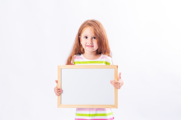 Little girl with long red hair is smiling and holding a white drawing board