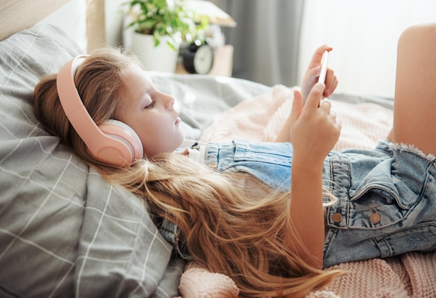 Little girl with mobile phone listening to music while lying in bed