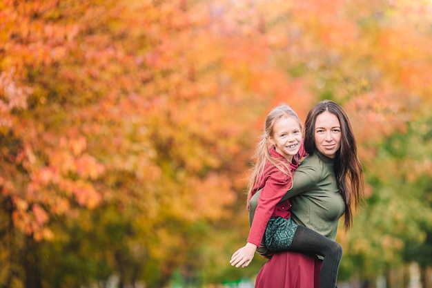 Little girl with mom outdoors in park at autumn day