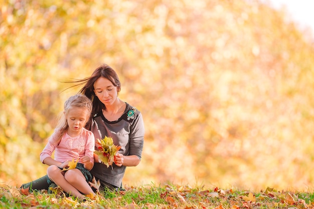 Little girl with mom outdoors in park at autumn day