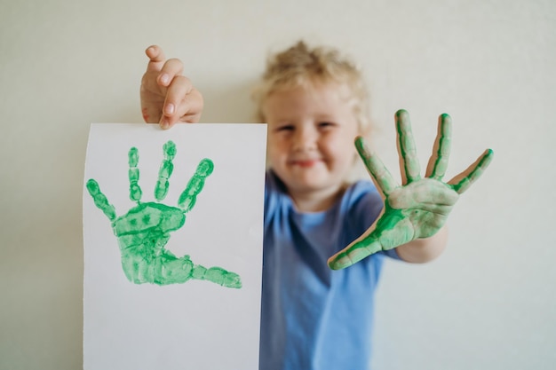 A little girl with a painted palm and a palm print on a sheet