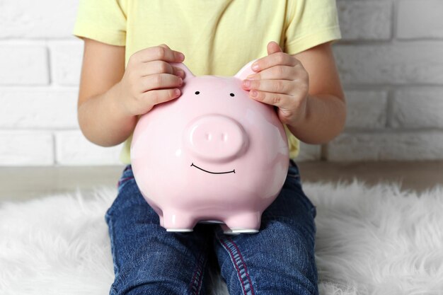 Little girl with the pig moneybox on brick wall background