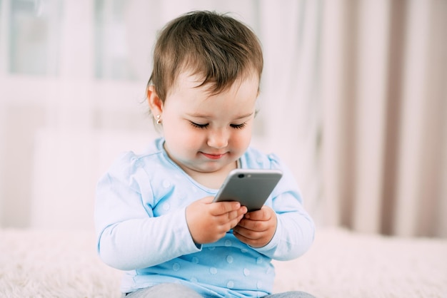 A little girl with a smartphone phone in her hands sits and presses very sweet