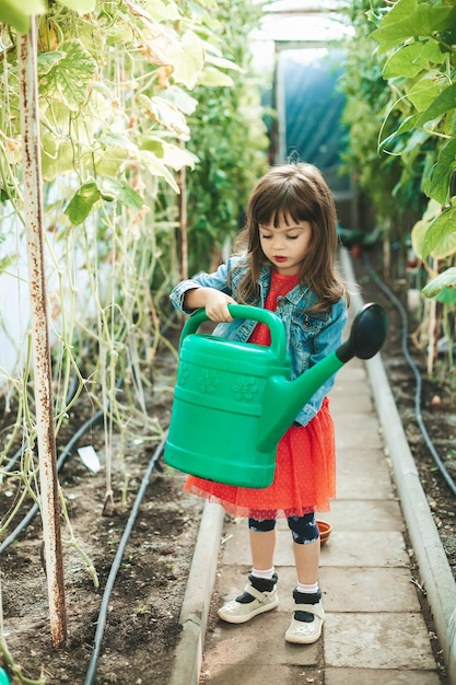 Little girl with a watering can in a greenhouse