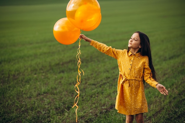 Little girl with yellow balloons in the field