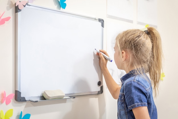 Photo little girl writing on empty whiteboard with a marker pen, learning, education and back to school concept