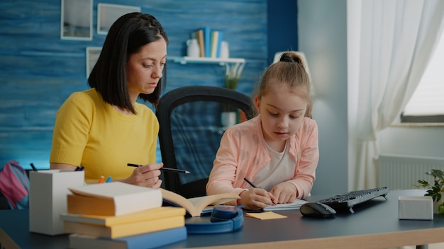 Little girl writing on notebook with pen while mother giving assistance