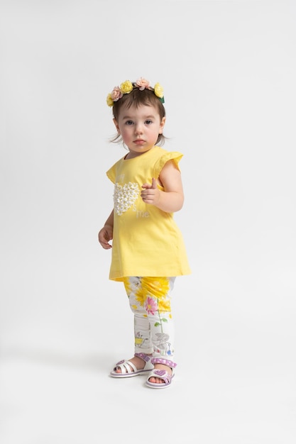 Little girl in a yellow casual children's dress with a wreath of flowers on her head posing on a white background