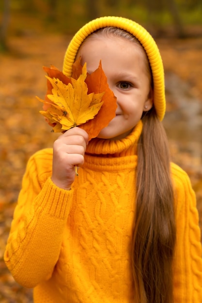 little girl in a yellow hat and sweater holds autumn leaves to her face urban autumn forest