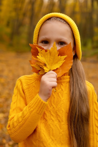 little girl in a yellow hat and sweater holds autumn leaves to her face urban autumn forest