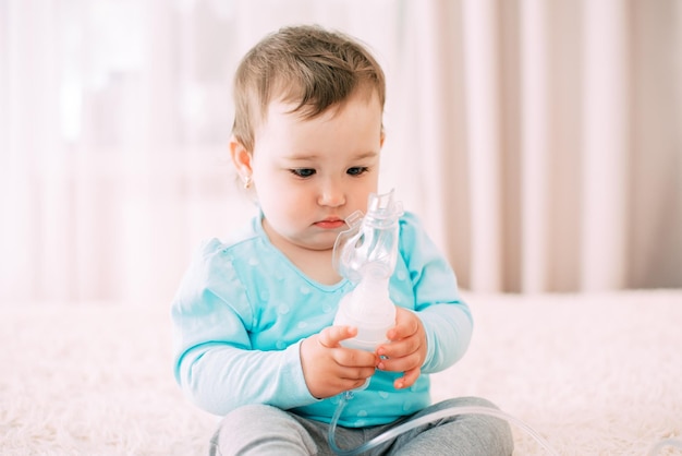 A little girl yourself holding the mask of the nebulizer, making inhalation very sweet