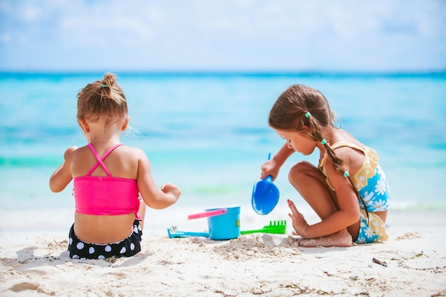 Little girls having fun at tropical beach playing together and making sandcastle