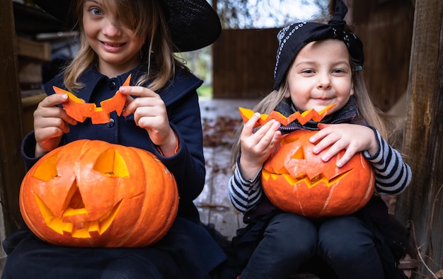 Little girls make jackolantern from big pumpkins for celebratiion of halloween holidayWitch costume hat coat Cut with knifetake out pulp with seedsOutdoors activity backyardChildren's party