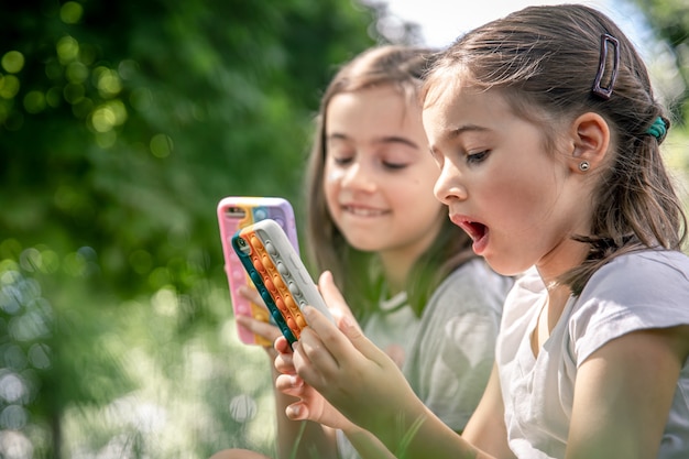 Little girls outdoors with phones in a case with pimples pop it, a trendy anti stress toy.