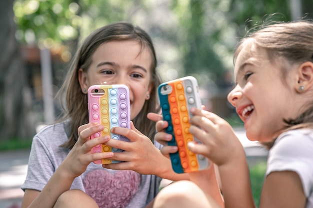 Little girls outdoors with phones in a case with pimples pop it, a trendy anti stress toy.