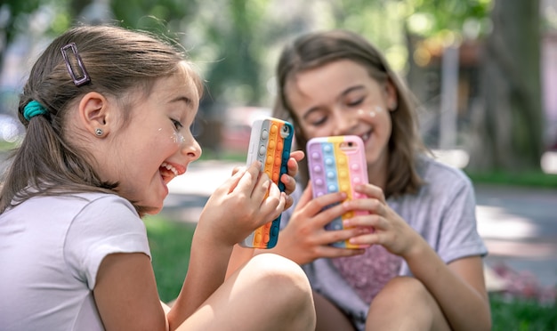 Little girls outdoors with phones in a case with pimples pop it, a trendy anti stress toy.