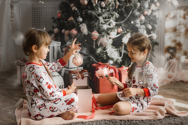 Little girls in pajamas open gift box under the Christmas tree