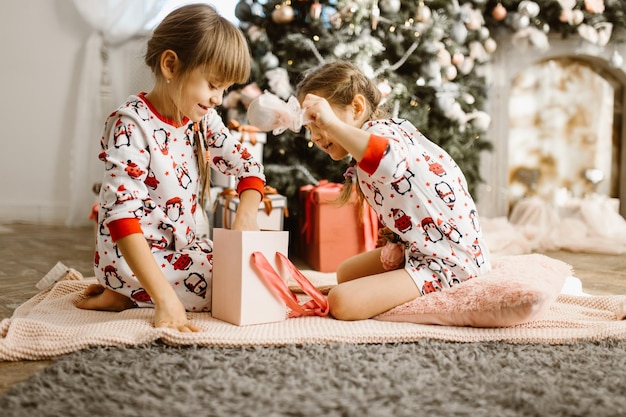 Little girls in pajamas open gift box under the Christmas tree