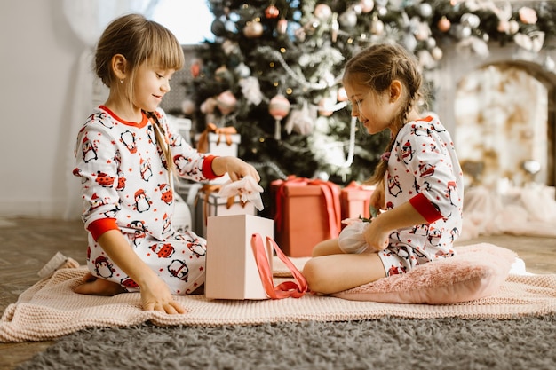 Little girls in pajamas open gift box under the Christmas tree