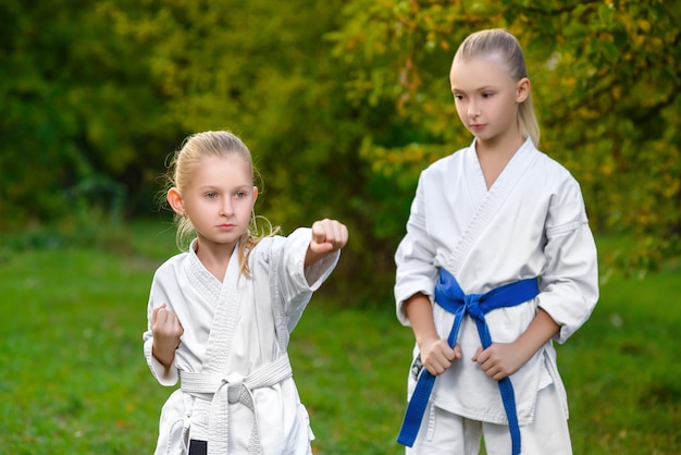 Little girls in white kimono during training karate exercises at summer outdoors