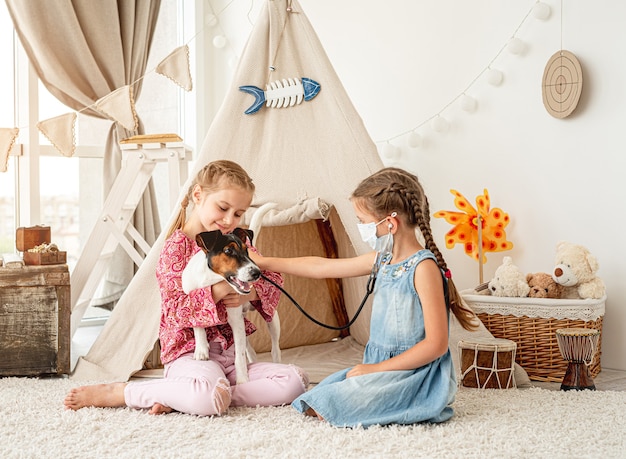 Little girls with phonendoscope listening dog like doctor sitting on floor in playroom