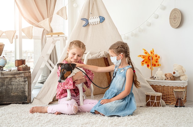 Photo little girls with phonendoscope listening dog like doctor sitting on floor in playroom