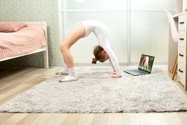 Little gymnast in a white leotard at home studying remotely Gymnastics lessons at home Gymnastics lessons online