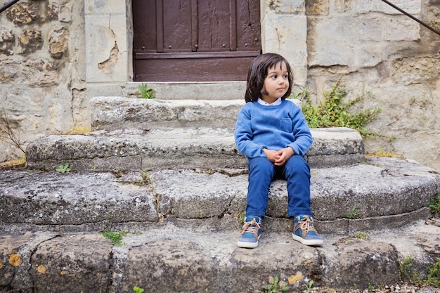 Little handsome baby boy sitting on ancient stone stairs outdoor