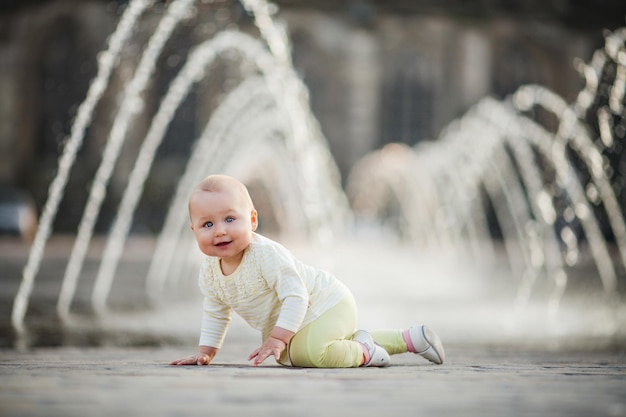 Little happy baby girl crawling on the square of the city near fountain