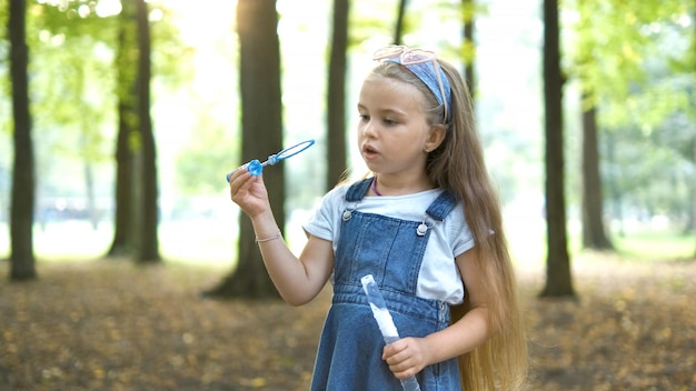 Little happy child girl blowing soap bubbles outside in green park Outdoor summer activities concept