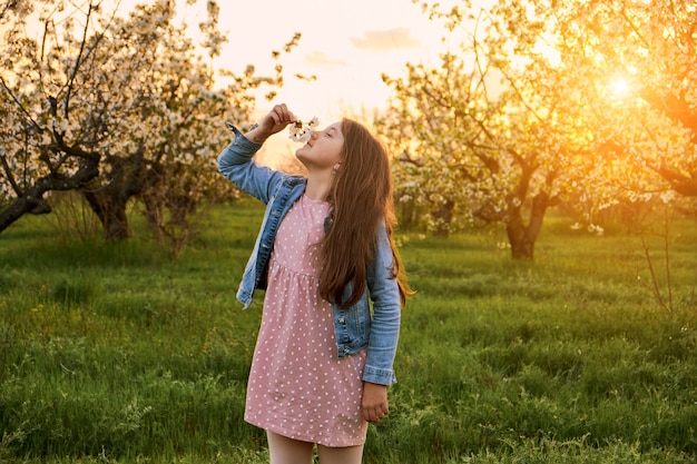 Little happy child girl playing under blooming apple trees with white flowers in blooming garden