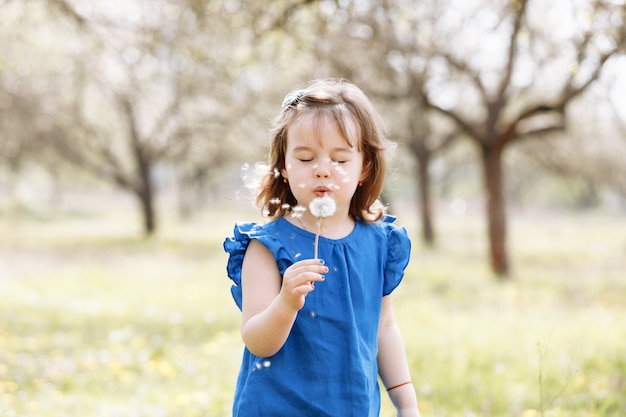 Little happy girl in a blue dress plays with flowers