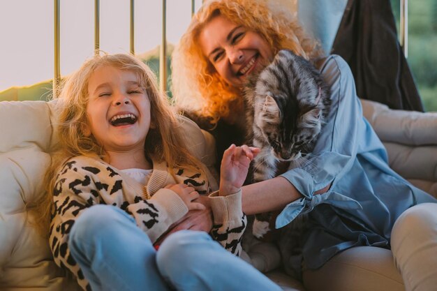 A little happy girl a child with a smile plays on a summer spring vernada at home with mom and a cat