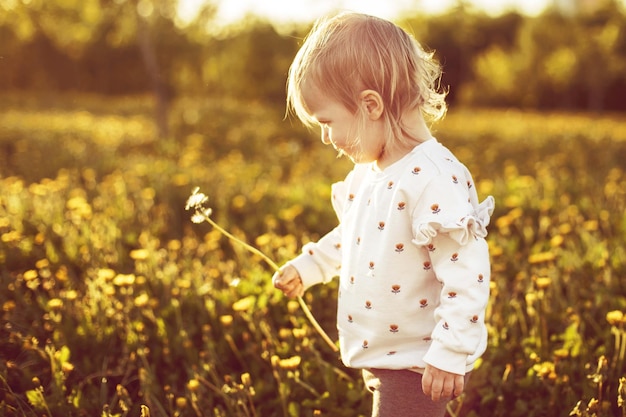 Photo little happy girl in a field with a dandelion in hand