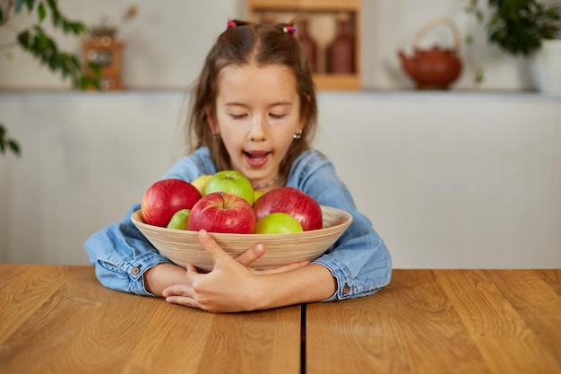 Little happy girl hold bowl with fruits in the kitchen at home healthy child snack Healthy food at home love fruit and vitamins