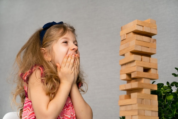 A little happy girl is playing the board game jenga at the table construction of a tower made of