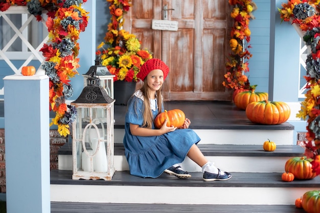 Little happy girl is sitting next to pumpkins near on house porch