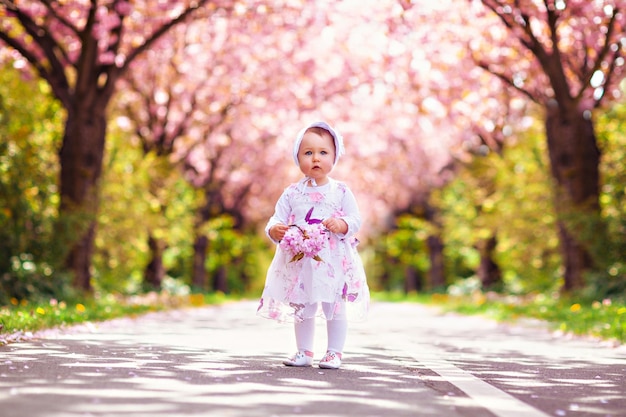 Little happy girl playing under blooming cherry tree with pink flowers in a beautiful spring garden