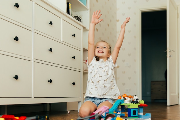 Little happy girl playing with colorful toy blocks. Educational and creative toys and games for young children. Playtime and mess in kid's room