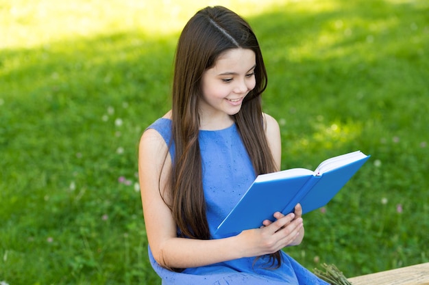 Little happy girl reading book outdoors sunny day cool story concept