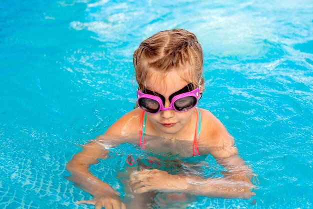 Little happy girl swims in the pool. summer holidays. girl in a swimsuit and swimming glasses.