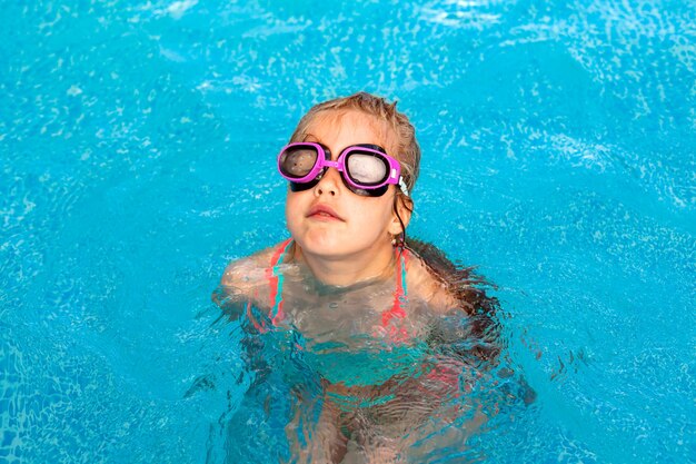 Little happy girl swims in the pool. summer holidays. girl in a swimsuit and swimming glasses.