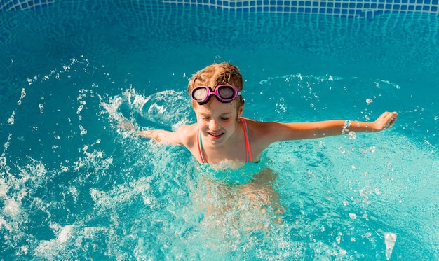 Little happy girl swims in the pool. summer holidays. girl in a swimsuit and swimming glasses.