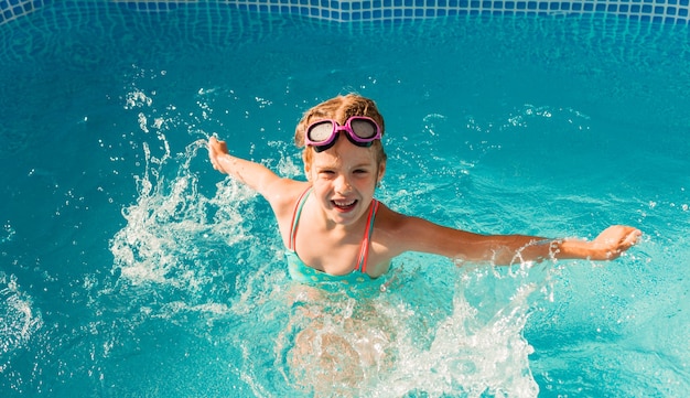 Little happy girl swims in the pool. summer holidays. girl in a swimsuit and swimming glasses.