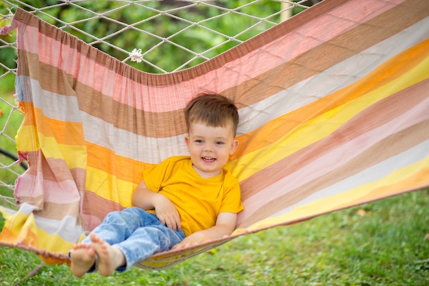 Little happy kid boy riding in a bright hammock in his park. Summer children's holiday