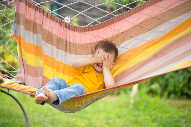 Little happy kid boy riding in a bright hammock in his park. Summer children's holiday